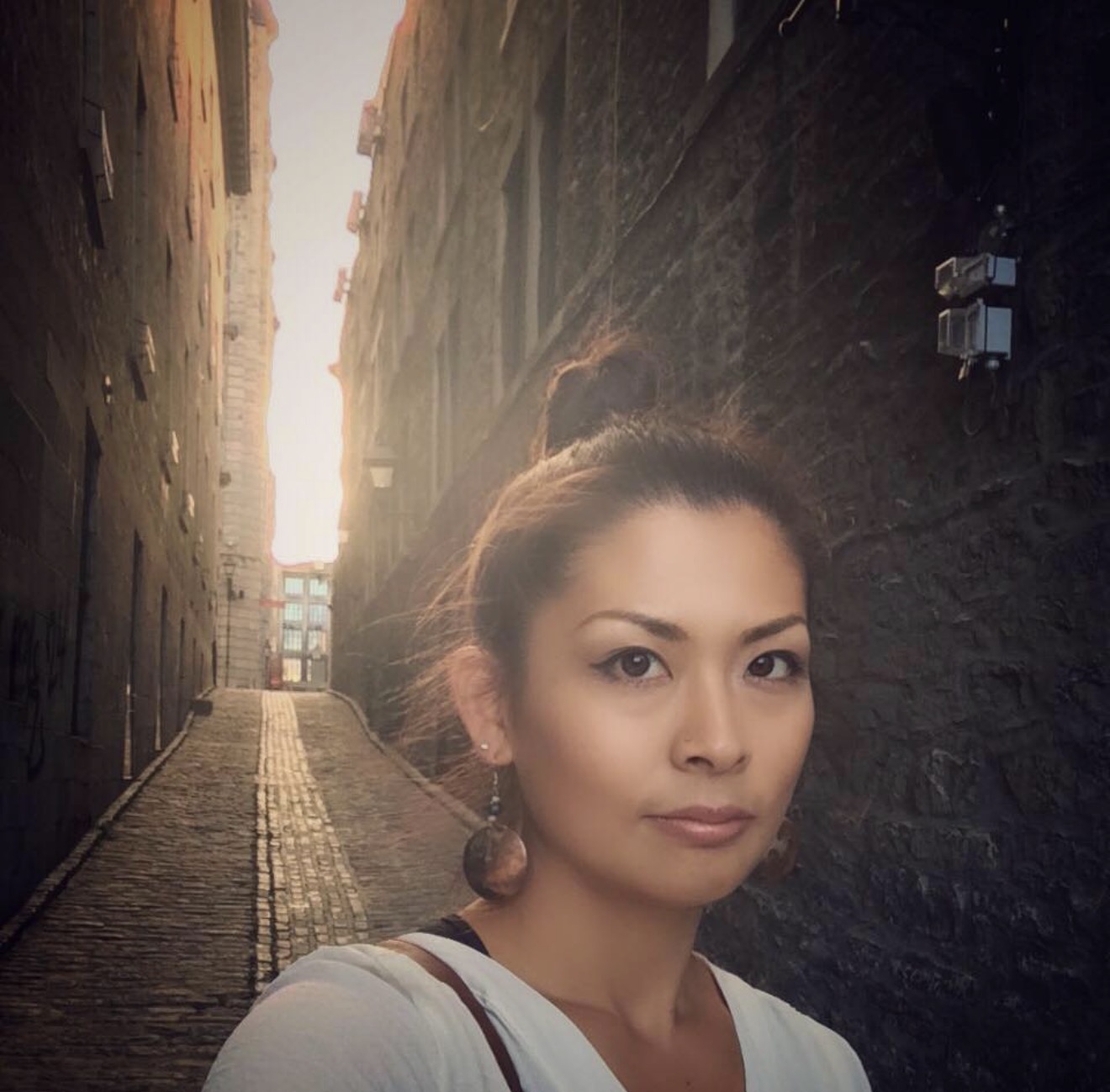 Ikumi in a white top in a cobblestone alley at golden hour